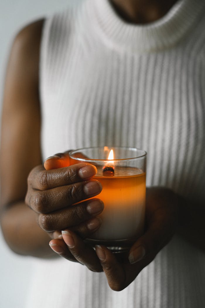 services-04 Crop anonymous black female standing with burning candle in glass for aromatherapy at home