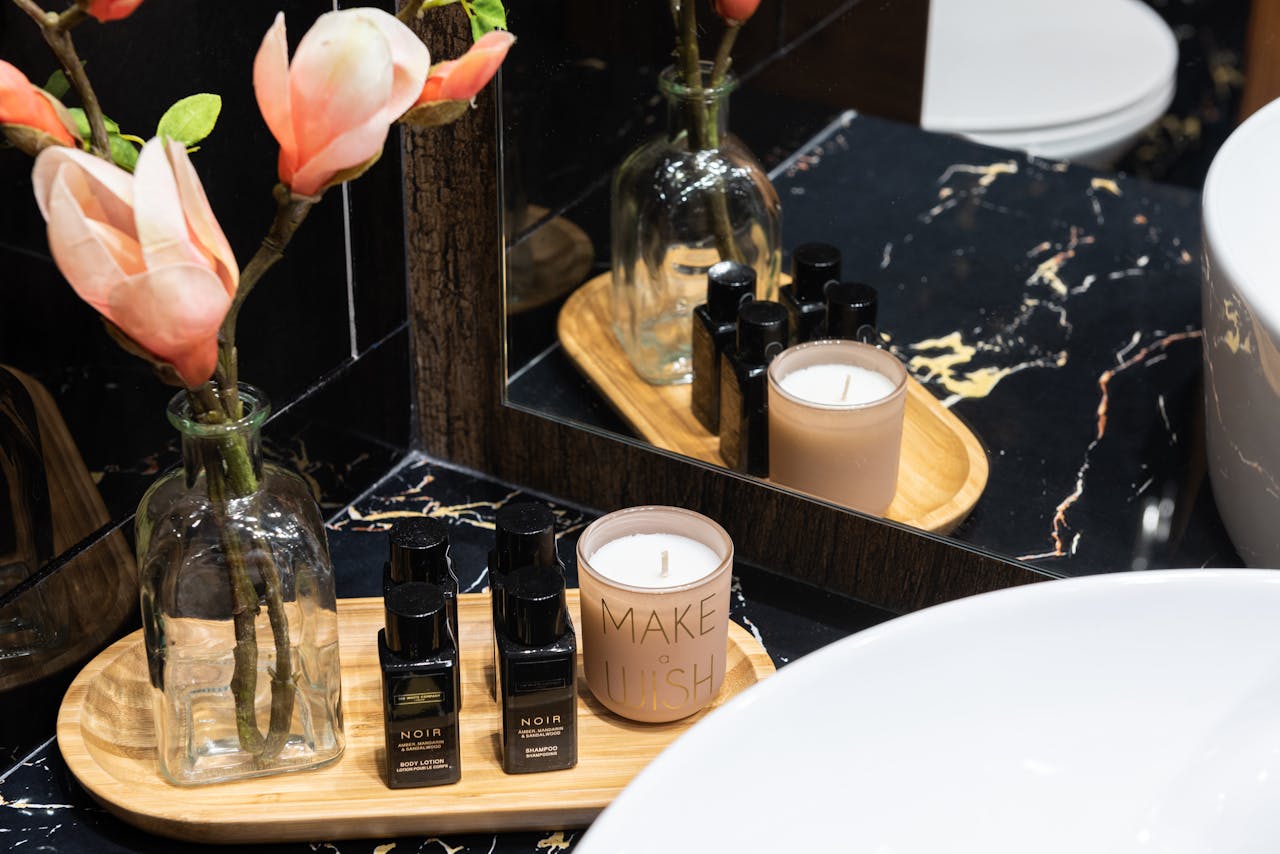 Set of beauty products in bottles between candle and artificial flowers in vase reflecting in mirror at home