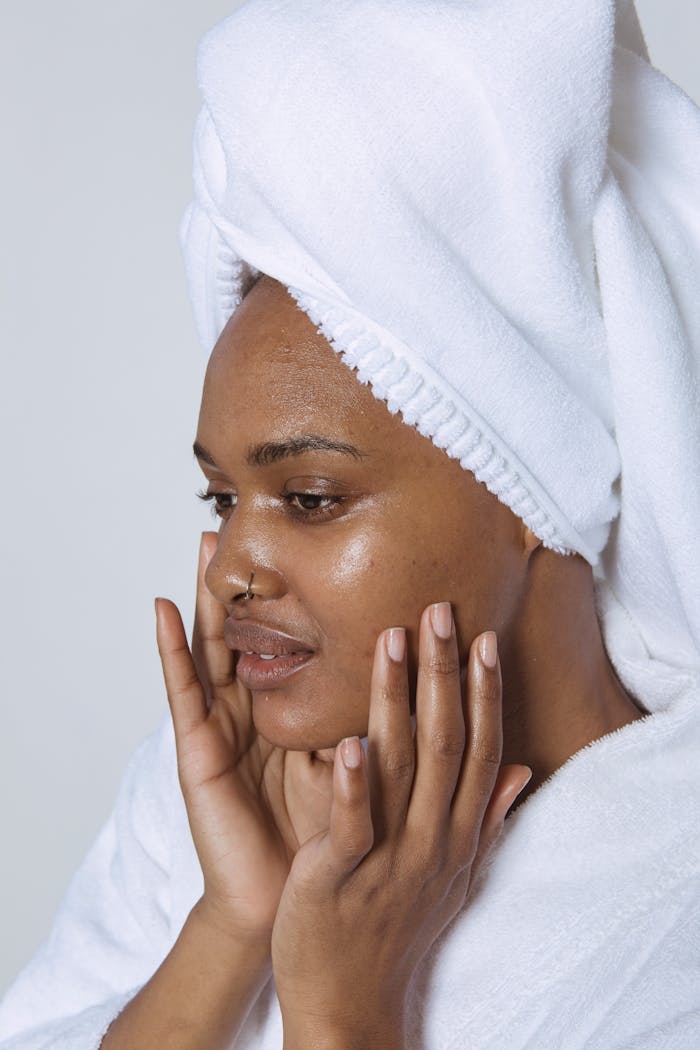 trusted-partner A serene woman applies skincare products with a bathrobe and towel wrap, promoting healthy skin.